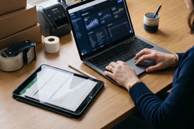 A workspace with a laptop, stacked shipping boxes, and a label printer