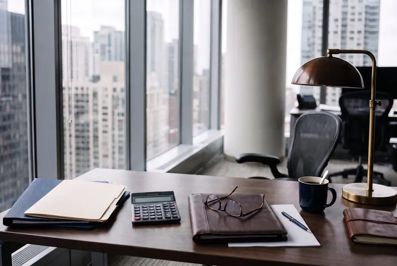 Document folders, a desk calculator, and reading glasses arranged on an office desk